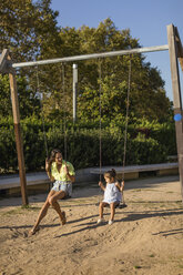 Glückliche Mutter und Tochter auf einer Schaukel auf einem Spielplatz - MAUF02434