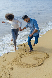 Spanien, Barcelona, glückliches Paar, das sich am Strand amüsiert und ein Herz in den Sand zeichnet - BOYF01278