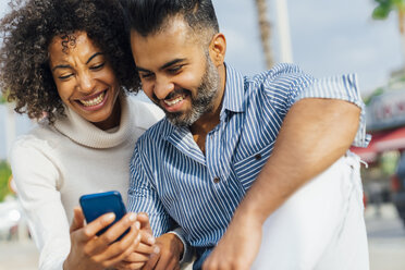 Glückliches Paar schaut auf Handy im Freien - BOYF01297