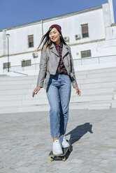 Porträt einer lächelnden jungen Frau, die auf ihrem Skateboard steht - KIJF02205