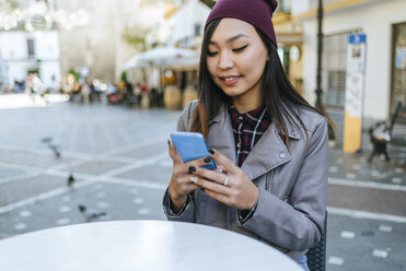 Porträt einer jungen Frau, die in einem Straßencafé ihr Smartphone benutzt - KIJF02220