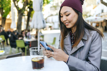 Lächelnde junge Frau mit Smartphone in einem Straßencafé - KIJF02222