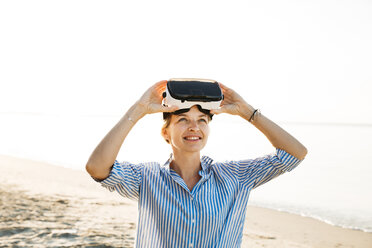 Porträt einer lächelnden Frau mit Virtual-Reality-Brille am Strand - HMEF00184