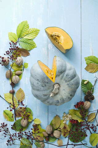 Herbstliches Arrangement mit geschnittenem Kürbis 'Crown Prince', Nüssen, Hagebutten und Herbstblättern, lizenzfreies Stockfoto