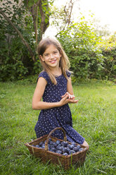 Porträt eines lächelnden Mädchens auf einer Wiese mit einem Weidenkorb voller Pflaumen - LVF07680