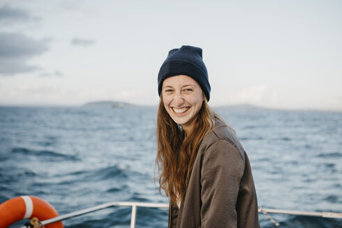 South Africa, young woman with woolly hat smiling during boat trip at sunset - LHPF00388
