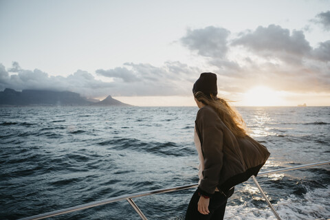 Südafrika, junge Frau mit Wollmütze während einer Bootsfahrt bei Sonnenuntergang, lizenzfreies Stockfoto