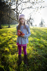 Porträt eines lächelnden Mädchens, das auf einer Wiese mit gesammelten Äpfeln im Herbst steht - LVF07692