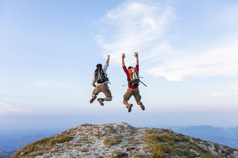 Italien, Monte Nerone, zwei glückliche und erfolgreiche Wanderer, die auf den Gipfel eines Berges springen, lizenzfreies Stockfoto