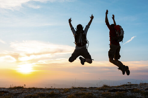 Italy, Monte Nerone, two happy and successful hikers jumping on top of a mountain at sunset - WPEF01322