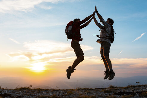 Italy, Monte Nerone, two happy and successful hikers jumping in the mountains at sunset - WPEF01323
