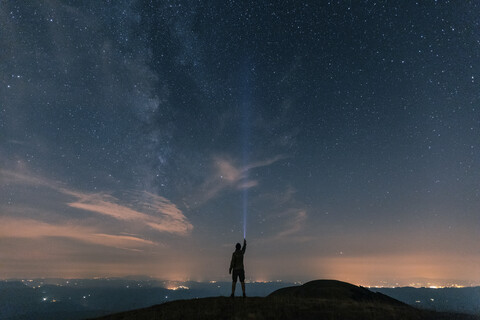 Italy, Monte Nerone, silhouette of a man with torch under night sky with stars and milky way stock photo