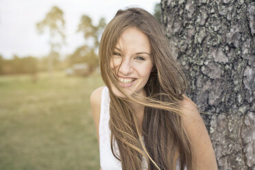 Porträt einer lachenden jungen Frau, die sich an einen Baumstamm lehnt - PNEF01179