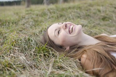 Lachende junge Frau auf einer Wiese liegend - PNEF01180