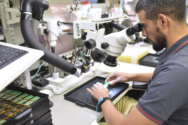 Mann, der ein Mikroskop für die Qualitätskontrolle bei der Herstellung von Leiterplatten für die Elektronikindustrie benutzt - LYF00879