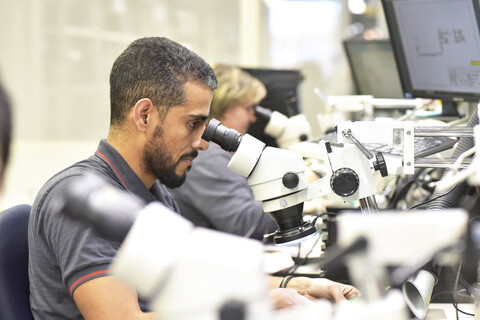 Man using a microscope for the quality control in the manufacturing of circuit boards for the electronics industry stock photo