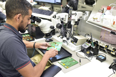Mann, der ein Mikroskop für die Qualitätskontrolle bei der Herstellung von Leiterplatten für die Elektronikindustrie benutzt - LYF00889