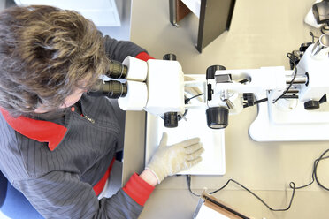 Frau, die ein Mikroskop für die Qualitätskontrolle bei der Herstellung von keramischen Leiterplatten für die Elektronikindustrie verwendet - LYF00902