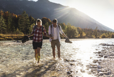 Austria, Alps, couple on a hiking trip wading in a brook - UUF16537