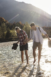 Austria, Alps, couple on a hiking trip wading in a brook - UUF16539