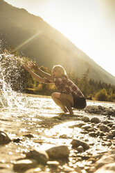 Austria, Alps, happy woman on a hiking trip splashing with water at a brook - UUF16543