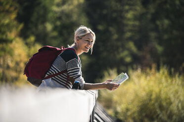 Österreich, Alpen, Junge Frau mit Rucksack auf Brücke lehnend, Karte haltend - UUF16564