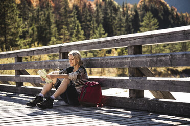 Österreich, Alpen, junge Frau mit Rucksack auf einer Brücke sitzend und eine Pause machend - UUF16567