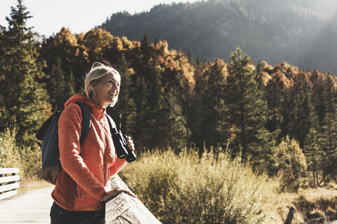 Austria, Alps, woman on a hiking trip standing on a bridge with binoculars stock photo