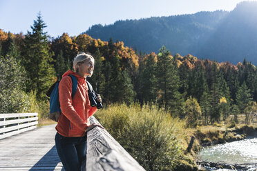 Austria, Alps, woman on a hiking trip standing on a bridge with binoculars - UUF16587