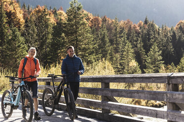 Österreich, Alpen, Paar mit Mountainbikes beim Überqueren einer Brücke - UUF16591