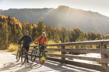 Österreich, Alpen, Paar mit Mountainbikes beim Überqueren einer Brücke - UUF16592