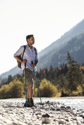 Österreich, Alpen, Mann beim Wandern auf Kieselsteinen an einem Bach stehend - UUF16602