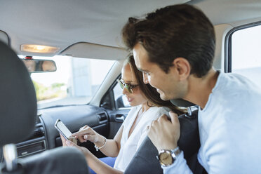 Couple in car with man on back seat and woman with cell phone on front passenger seat - KIJF02229