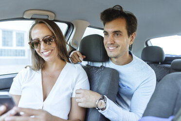 Happy couple in car with man on back seat and woman with cell phone on front passenger seat - KIJF02232