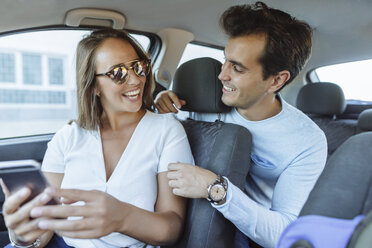 Happy couple in car with man on back seat and woman with cell phone on front passenger seat - KIJF02233