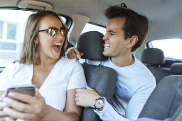 Glückliches Paar im Auto mit Grimassen schneidendem Mann auf dem Rücksitz und Frau auf dem Beifahrersitz - KIJF02235