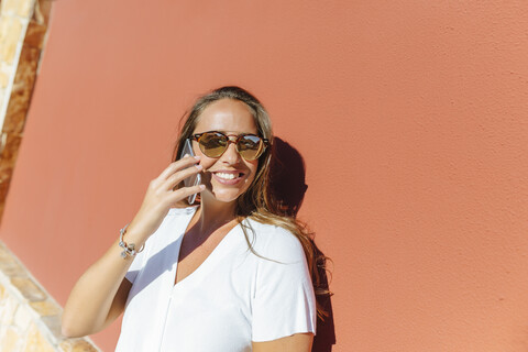 Lächelnde Frau am Mobiltelefon an einem sonnigen Tag, lizenzfreies Stockfoto