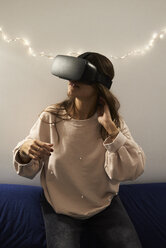 Junge Frau mit VR-Headsets, die nachts zu Hause auf dem Sofa Spiele spielt - IGGF00731