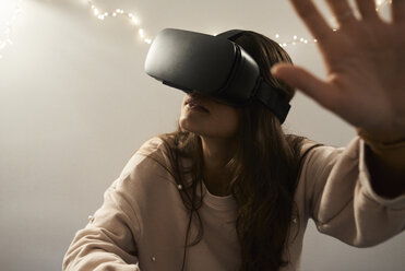 Young woman using VR headsets playing games on the sofa at home at night - IGGF00733