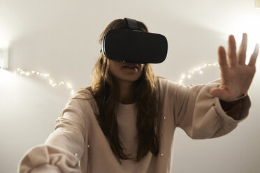 Junge Frau mit VR-Headsets, die nachts zu Hause auf dem Sofa Spiele spielt - IGGF00734