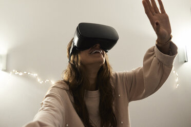 Junge Frau mit VR-Headsets, die nachts zu Hause auf dem Sofa Spiele spielt - IGGF00735