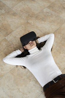 Young woman using virtual reality headsets lying on the floor at home - IGGF00741