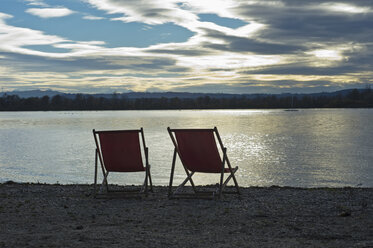 Germany, two empty deckchairs standing at lakeshore of Ammersee by sunset - CRF02822