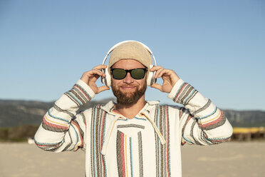 Mann mit Kopfhörern und Sonnenbrille am Strand - KBF00466