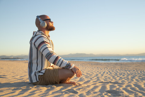 Mann mit Kopfhörern am Strand sitzend, lizenzfreies Stockfoto