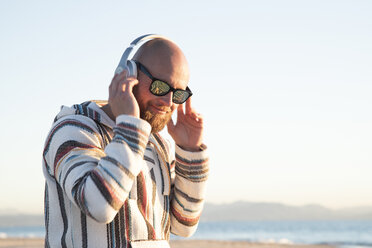 Mann mit Kopfhörern und Sonnenbrille am Strand - KBF00471