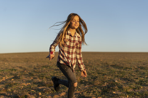 Porträt eines lächelnden Mädchens mit Lutscher, das bei Sonnenuntergang auf einer Weide läuft, lizenzfreies Stockfoto