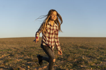 Portrait of smiling girl with lollipop running on pasture by sunset - ERRF00673