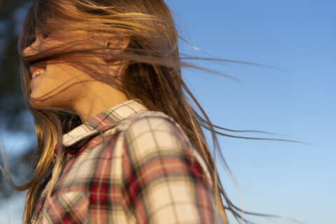 Profile of laughing girl with blowing hair against blue sky stock photo