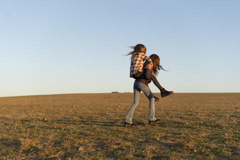 Girl giving her sister a piggyback ride outdoors stock photo